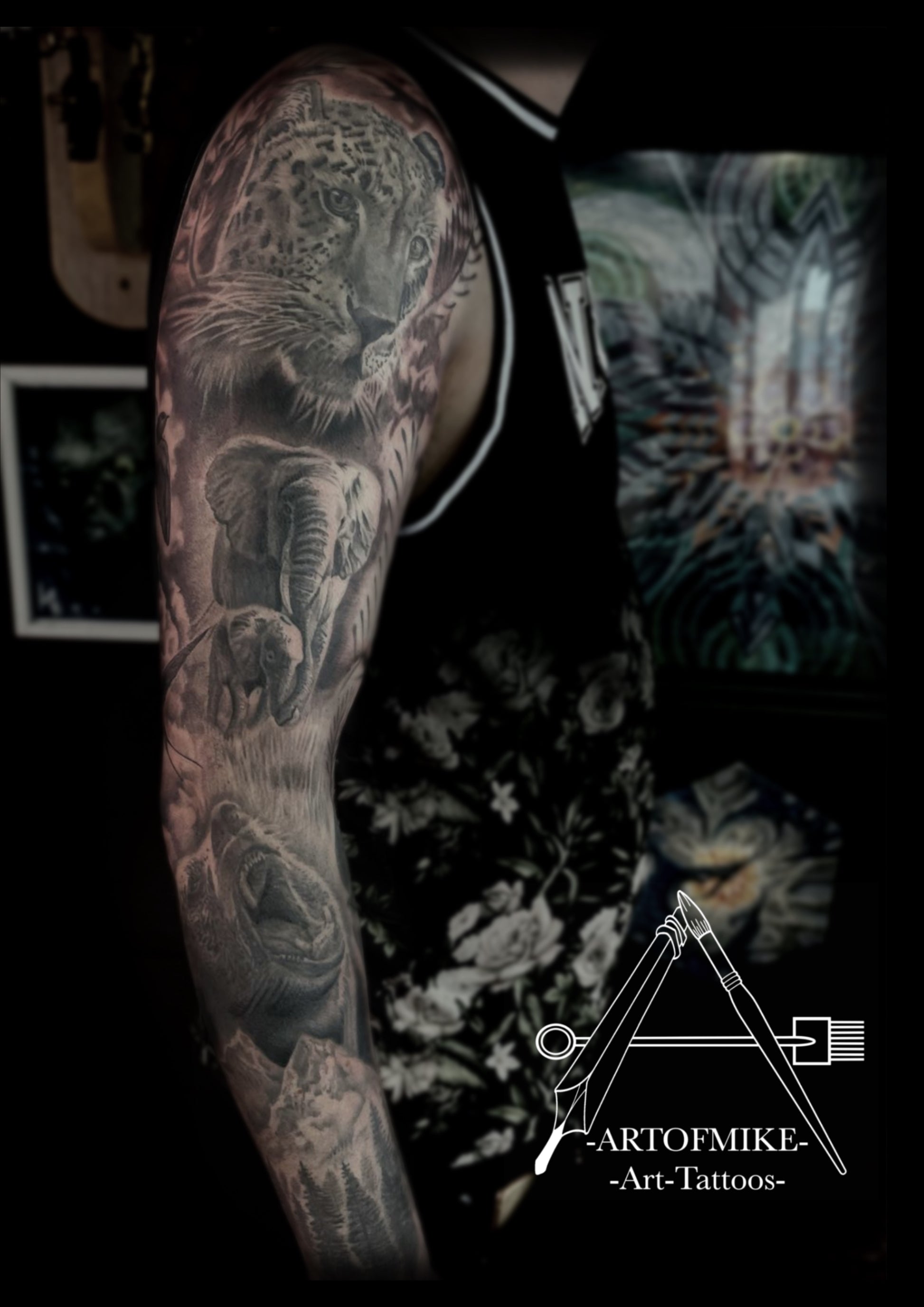 A person’s arm with a black and grey sleeve tattoo of a leopard, elephants, and rhinoceros at a Shrewsbury studio. “Book your Tattoo now with Artofmike @innerdarkness” by Artofmiketattoos.com logo in the corner.