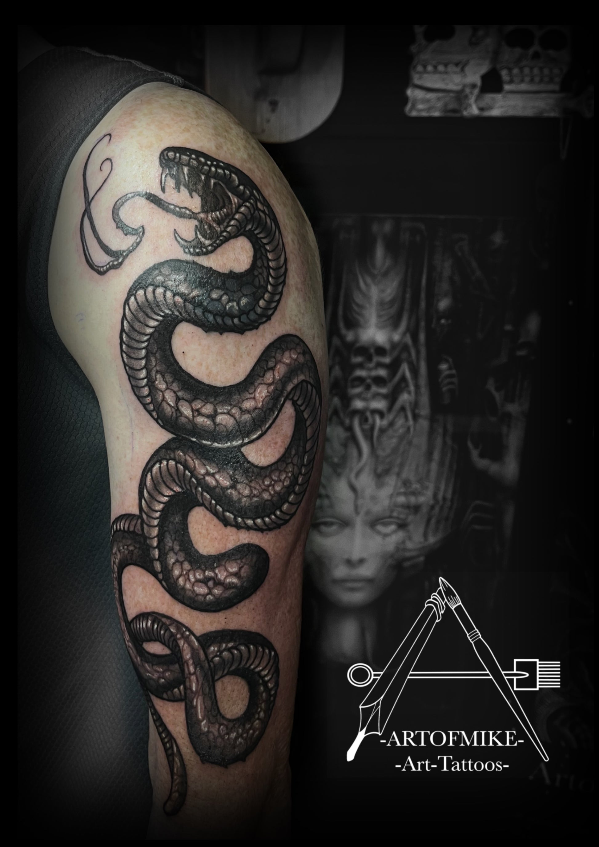 A detailed black and gray coiled snake tattoo on an upper arm, with surreal art and “ARTOFMIKE -Art-Tattoos-” logo in the background. Book your tattoo now with Artofmiketattoos.com for your next studio consultation.